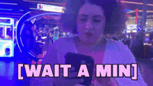 a woman is looking at her phone and the words wait a min are on the screen