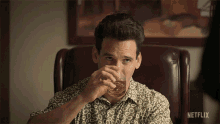a man sits in a chair drinking from a glass with netflix written on the bottom