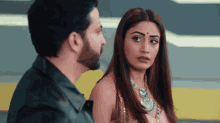 a man and a woman are looking at each other with the woman having a red dot on her forehead
