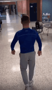 a man in a blue under armour shirt and grey sweatpants is walking down a hallway .