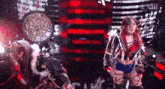 two women are standing on a stage with a dartboard in the background .