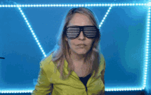a woman wearing a yellow jacket and striped sunglasses makes a funny face