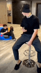 a man is sitting on a bar stool looking at his phone while another man sits on a blue bean bag chair
