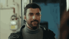 a man with a beard wearing a turtleneck sweater and a leather jacket .