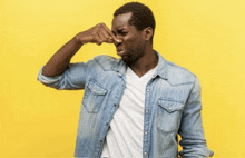 a man in a denim shirt is covering his nose against a yellow background .