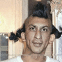 a man with a mohawk and pigtails on his head is looking at the camera .