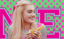 a woman is eating a sandwich in front of a pink and green background with the letter n on it .