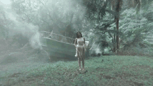 a woman in a white dress is standing in front of a boat in the woods