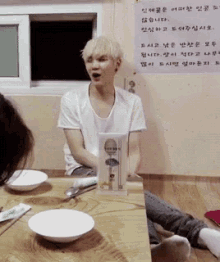 a man sitting at a table with a sign on the wall that says ' korean '