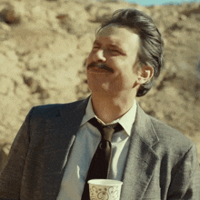 a man in a suit and tie holds a paper cup