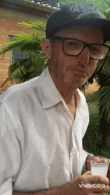 an older man wearing glasses and a hat is holding a glass of water