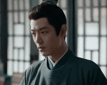 a man in a green robe is standing in front of a window .