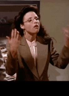 a woman in a suit and glasses is waving her hands