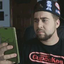 a man wearing a johnny cupcakes shirt holds a cell phone