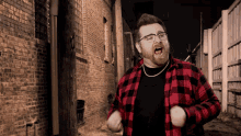 a man wearing glasses and a plaid shirt is standing in front of a brick building