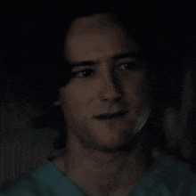 a close up of a man 's face in a dark room wearing a blue scrub top .