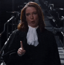 a woman in a judge 's robe and white lace tie is giving a thumbs up .