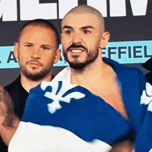 a man with a beard is holding a blue and white flag with a fleur de lis on it