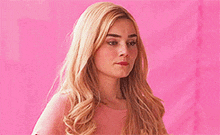 a blonde woman in a pink shirt is standing in front of a pink wall .