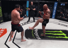 a man kicking another man in a boxing ring with monster energy on the floor