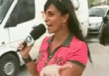 a woman in a pink shirt is talking into a microphone while holding a piggy bank .