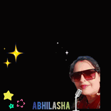 a woman wearing sunglasses stands in front of a sign that says " good luck abhilasha "