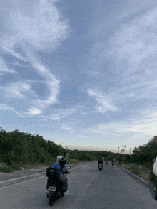 a group of people riding motorcycles down a road with a blue sky in the back