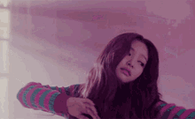 a woman with long hair is wearing a pink and green striped sweater and looking at the camera .