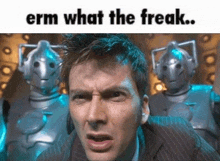 a man in a suit is standing in front of two robots and making a funny face .