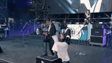 a man playing a guitar and a woman playing a guitar on a stage with a sign that says le