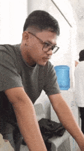 a man wearing glasses and a grey shirt is standing in front of a water cooler