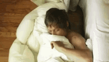 a man is sleeping in a bed with a white comforter and blanket .