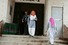 a woman in a hijab walks down stairs in front of a building with the word tower on it