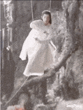a man in a white dress is hanging from a rope on a tree branch .