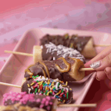 a person holding a banana covered in chocolate and sprinkles on a pink tray