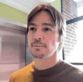 a man with a beard and a yellow sweater is looking at the camera .