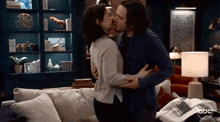 a man and a woman kissing in a living room with abc written on the corner