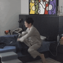 a woman is jumping on a bed in front of a painting of teletubbies