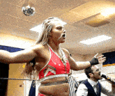a woman in a red top is standing in a ring with a referee and a man singing into a microphone