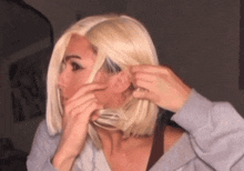 a woman wearing a blonde wig is covering her mouth with her hand