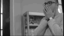 a man wearing glasses is covering his face with his hands