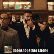 a man in a suit stands in a crowd with the words goons together strong on the bottom