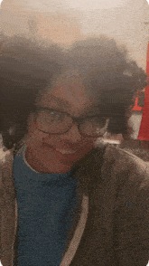 a woman wearing glasses and a blue sweater smiles for the camera