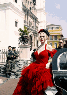a woman in a red dress stands in front of a building