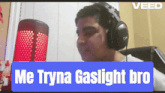 a man wearing headphones is sitting in front of a red lamp and a sign that says me tryna gaslight bro