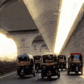 a row of rickshaws are driving under a bridge and one of them has the word rickshaw on it