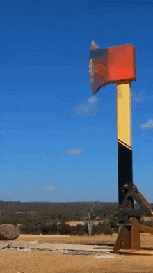 a large red yellow and black axe stands in a field