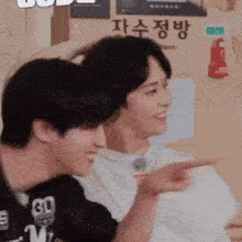 two young men are sitting next to each other and one is pointing at the other .