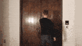 a man in a black shirt is standing in front of a wooden door with a light switch on the wall