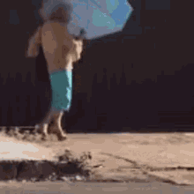 a shirtless man in blue shorts is holding an umbrella while walking down the street .
